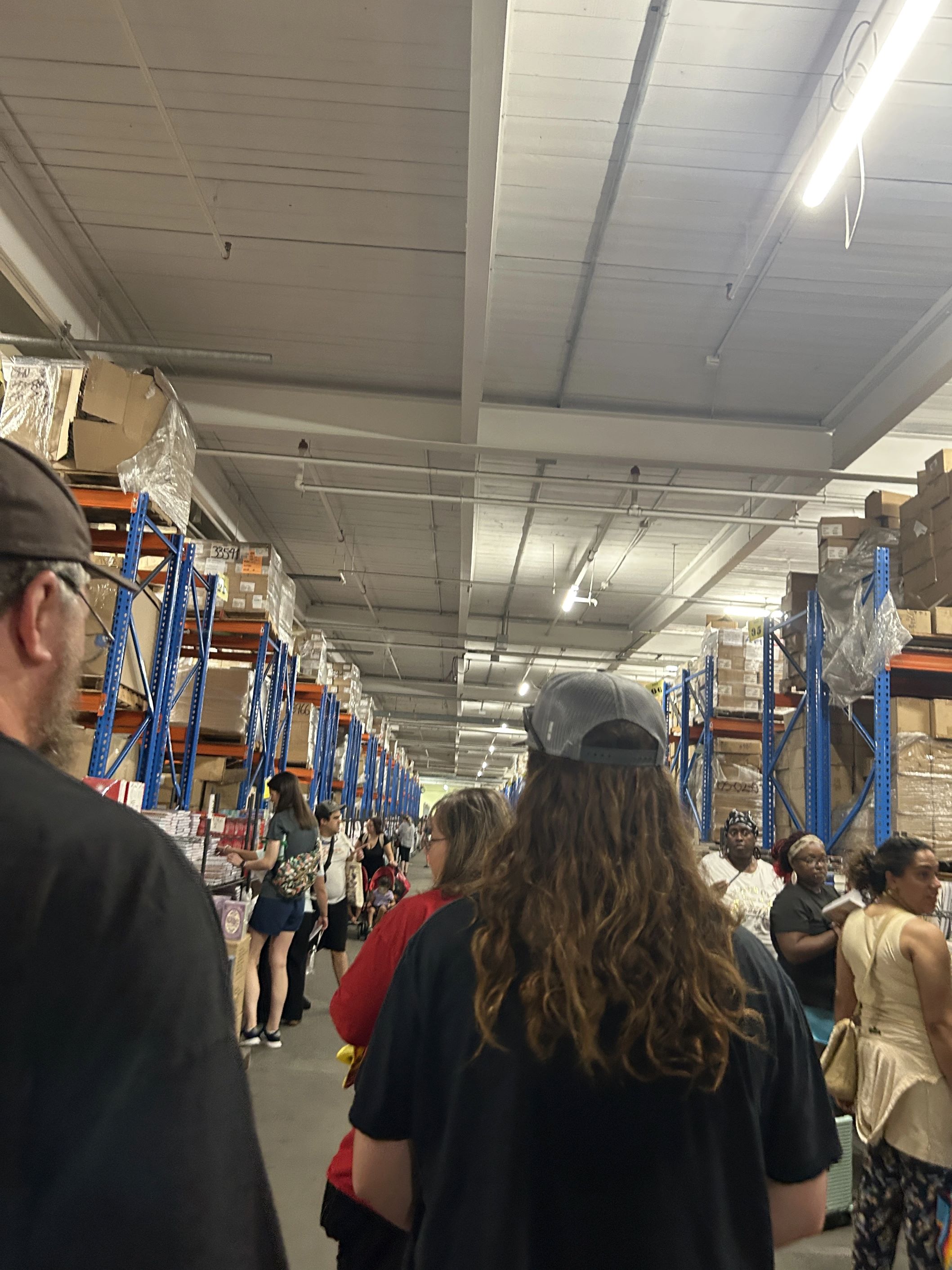 Image of people walking through a crowded warehouse with books everywhere on metal bookshelves.
